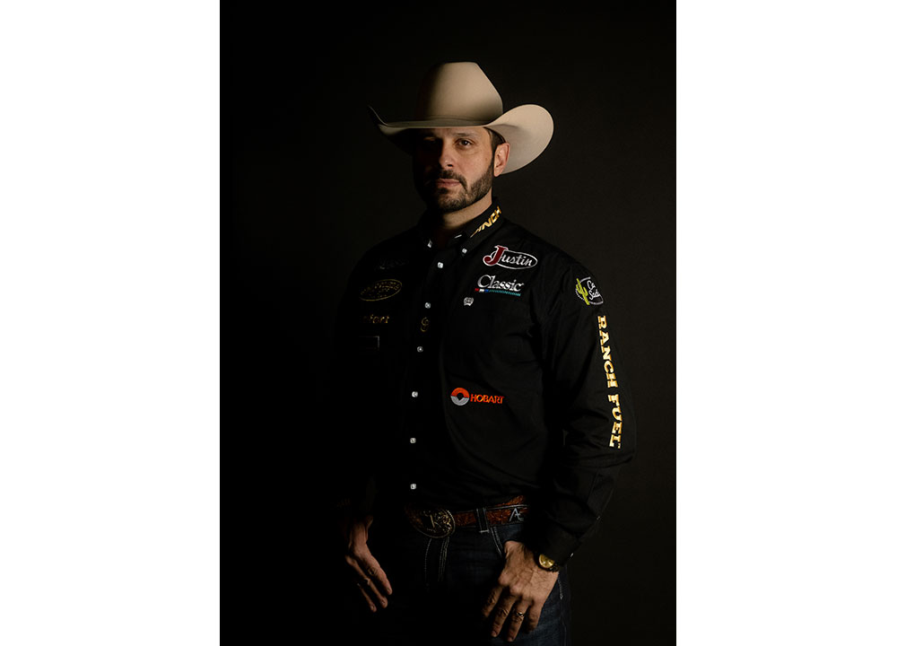 Anthony Lucia vistiendo una camisa negra y un sombrero de vaquero, mirando a la cámara con su rostro en sombras.